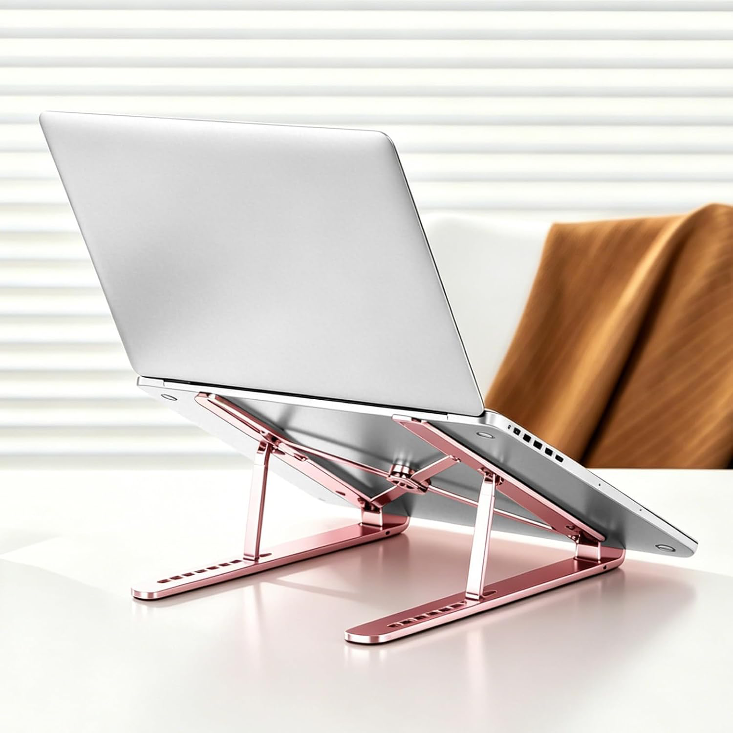 Rose Gold stand on a white desk holding an open silver laptop at a raised angle